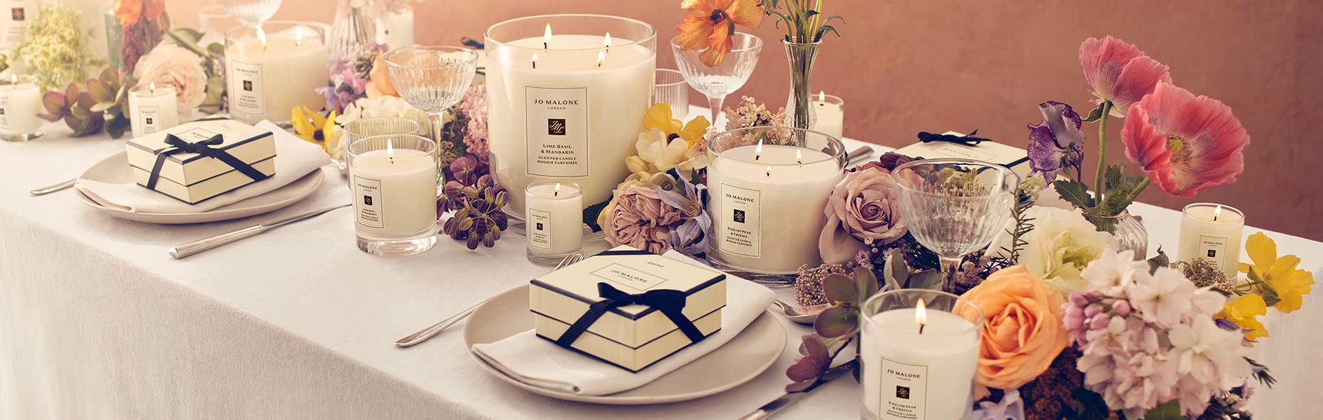 Image of a wedding dining table covered in flowers & candles with jo malone boxes on the plates for wedding favours